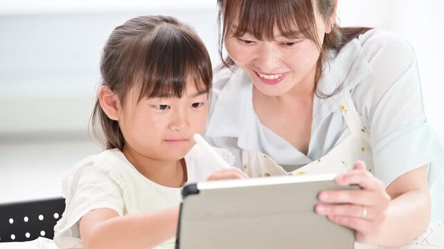 勉強がわかった！と見つめ合う喜ぶ、タブレットを使って一緒に学習する、教える母親と小学生の女の子・家庭で学ぶ親子のライフスタイルの動画　勉強が楽しい嬉しいイメージ