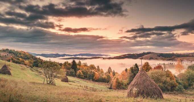 Breathtaking timelapse an autumn morning in Zakarpattia region of Ukraine. The sun rises over dramatic landscape, casting golden rays through heavy, moody clouds, while serene fog rolls through 