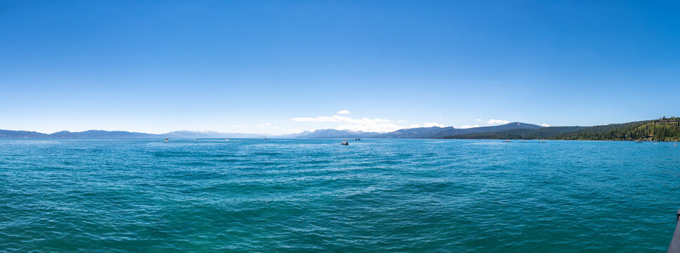 peaceful sailing on a serene lake surrounded by majestic mountains under a clear blue sky with white clouds and gray tones