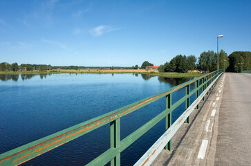 Fototapeta premium Bridge over the Dalälven river south of Hedesunda in Sweden, with calm water, green fields, and a clear blue sky