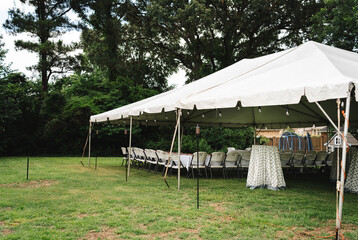 Large white event tent with tables and chairs set in a backyard © Trey