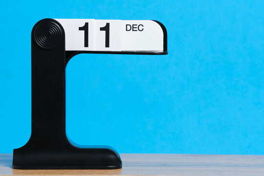 Modern flip calendar showing December 11 on wooden table with bright blue background.