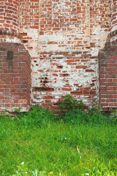 Green grass contrasts rough facade of the old red brick wall with weathered texture