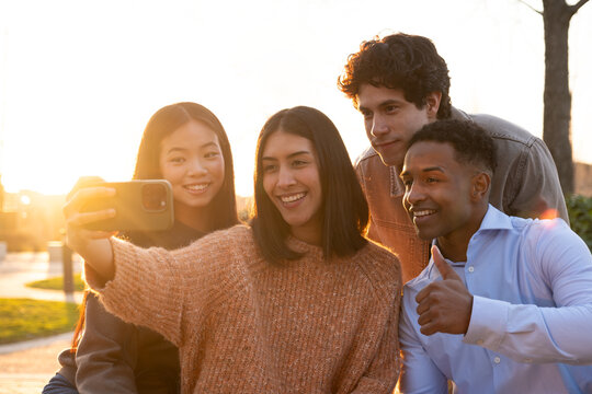 Diverse group of smiling friends holding smart phone and posing for a selfie outdoors