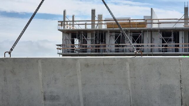Slow motion front shot of large concrete wall panel being tilted into vertical position by crane