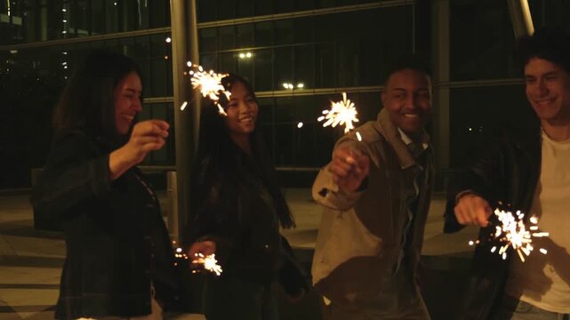 Joyful multiethnic friends having fun and celebrating with burning sparklers on a city rooftop