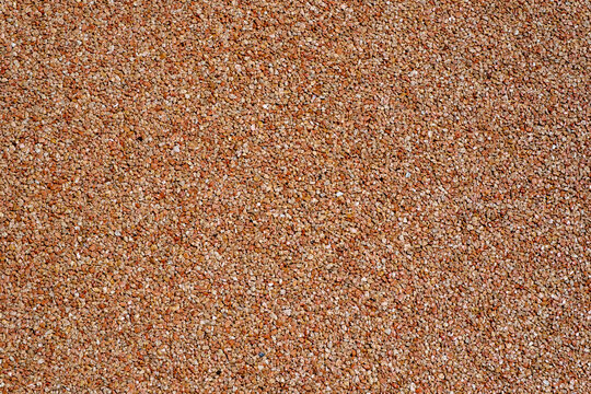 Close-up of a seamless exposed aggregate surface with warm terracotta and brown tones. A detailed texture showing small crushed stones and pebbles