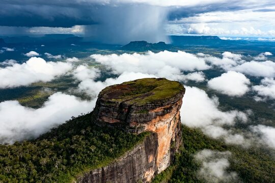 Aerial view of a towering tepui surrounded by clouds and lush greenery in a tropical landscape