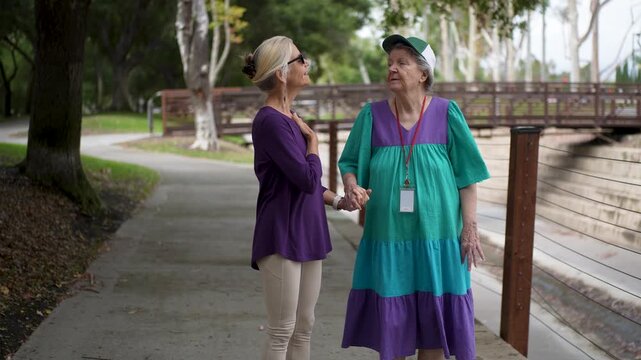 Mature daughter walks with her mother in a park, sharing smiles and stories while enjoying their time outdoors together