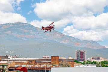 A red aerobatic biplane performing air shows in a blue sky with white clouds. Classic airplanes © Toni