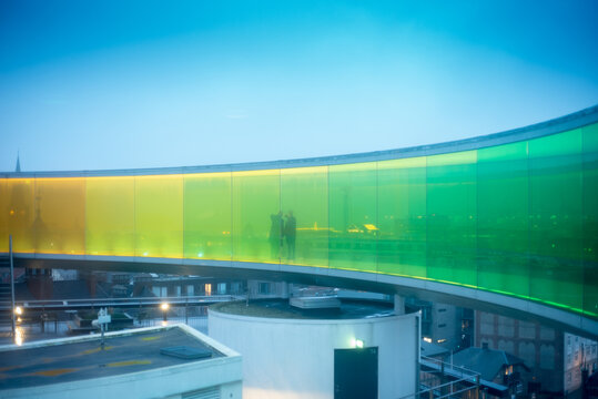 AARHUS, DENMARK &mdash; Visitors stand inside the colorful glass walkway of Your Rainbow Panorama at ARoS Aarhus Art Museum during blue hour,.
