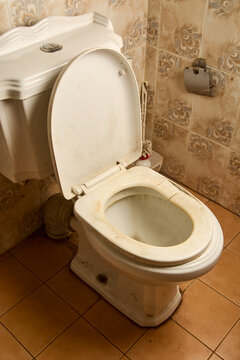 dirty old and broken white toilet seat in tiled bathroom, stained ceramic bowl with open lid, angle view with copy space, poor hygiene and plumbing maintenance concept