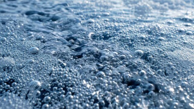 Close up of bubbling blue water surface with moving foam and sea spray, slow motion macro shot for nature and ocean concept