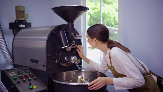 Female roaster smelling fresh beans at coffee roasting machine