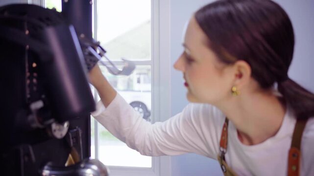 Female roaster smelling fresh beans at coffee roasting machine