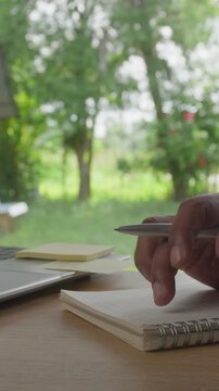 Close Up of Hand Tapping Finger on Notebook While Thinking with Laptop and Green Nature Bokeh Background, Decision Making and Creative Thinking Concept