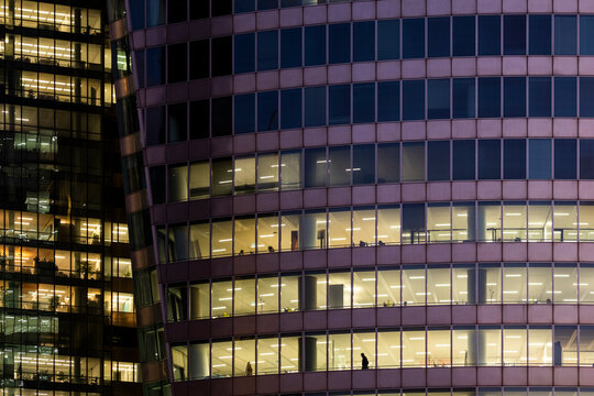 Office building facade at night reveals urban architecture through glass windows, where corporate interior floors glow across a curved exterior