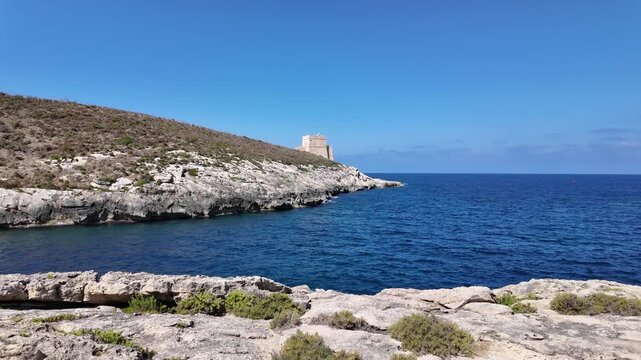 Low angle view of the Xlendi Tower standing against the azure sea and rugged coastline, creating a stunning contrast, Xlendi, Munxar, Malta. Hyperlapse. High quality 4k footage
