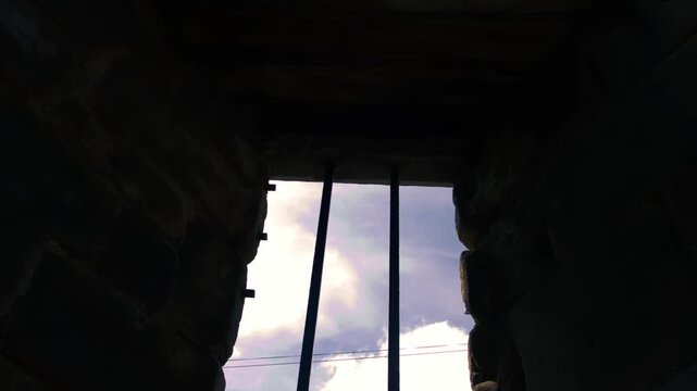 Prison bars on a stone wall silhouette against blue cloudy sky