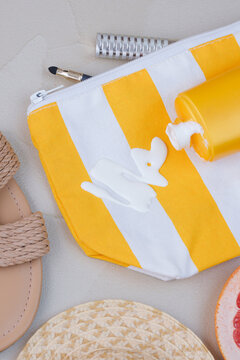 An open cosmetic bag with spilled sunscreen is surrounded by a straw hat, makeup brush, and cosmetic accessories on the sand. Concept of daily stains on clothing