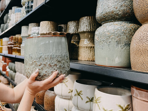 Person holds ceramic planter pot while choosing from large selection stacked on warehouse shelves. Modern pottery selection, ceramic planter pot, minimalist home decor, Choosing flower pots.