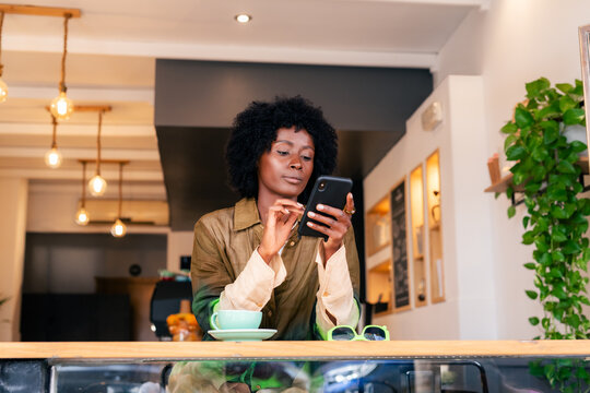 Woman Using Smartphone in Cafe While Sitting at Wooden Table