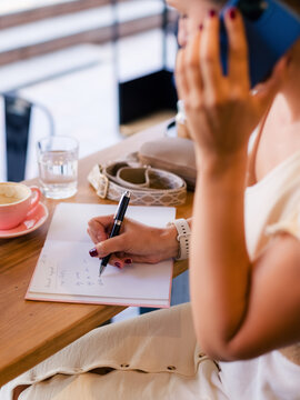 Woman having phone call at cafe and taking notes 