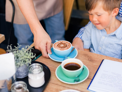 Child Receives Hot Drink From a Waiter in a Cafe 