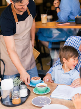 Waiter Serves Cocoa to Child at Cafe During Busy Brunch Time