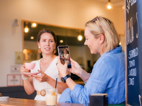 Women Sharing a Drink and Taking Photos at a Cafe