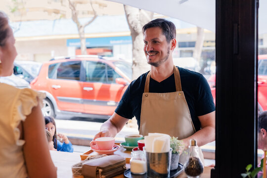 Smiling waiter serving his guests at cafe 