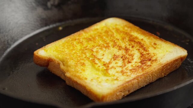 Close-up video of a slice of buttered white bread toasting on a hot cast iron skillet