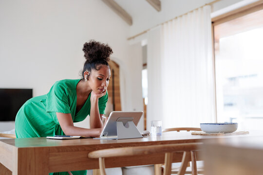 Woman in green dress works on digital tablet at home.