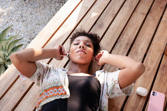 Woman relaxing on wooden deck with earbuds and phone.