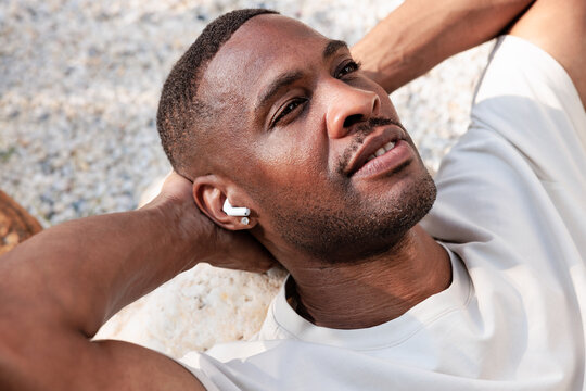 Man relaxing outdoors with earbuds, looking up.