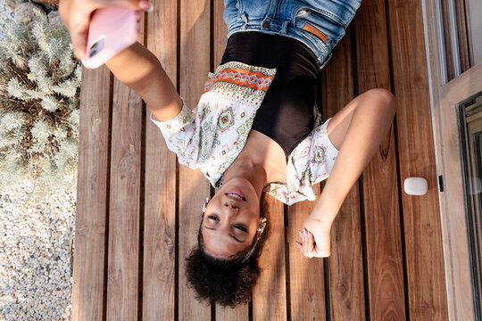 Woman takes selfie while lying on wooden deck.