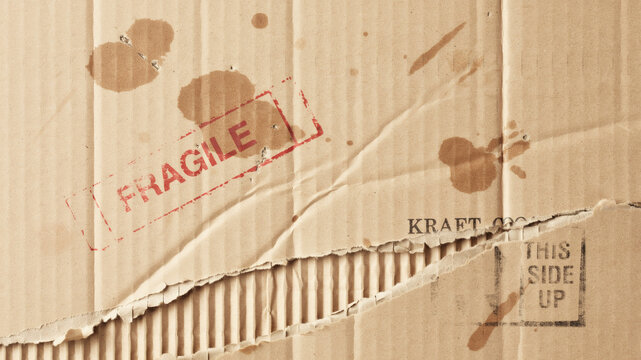 Weathered corrugated cardboard texture with fragile stamp, torn brown kraft paper background, damaged shipping box surface with water stains