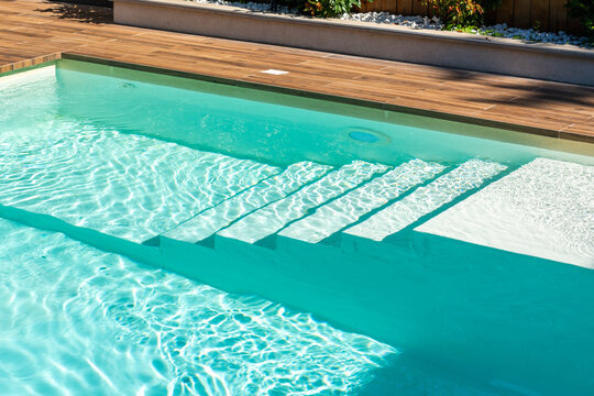 Modern swimming pool with turquoise water, elegant submerged steps, and natural wooden deck design