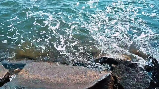 Ocean waves crashing against a concrete breakwater under a clear blue sky. The coastal protection structure stretches into the sea, creating a peaceful yet dynamic seascape with beautiful ocean views.