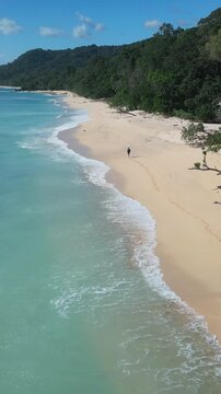 Asian woman hiking along remote beach drone perspective with mountain backdrop lush forest edge long curve of sand rhythmic waves footprints leading into distance adventurous, Java island