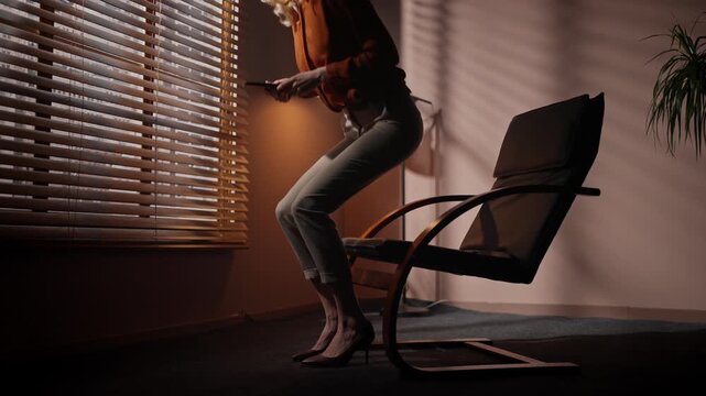 Professional woman going to office chair. Female sitting at chair at background of dim room design. Woman in official suit sitting at dark room. Casting director holding tablet at audition room.