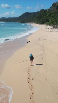 Walking along vibrant coastline. Serene woman strolls by emerald water with gentle waves. Peaceful woman walks along turquoise shore with reflected sky and distant forest, vertical video