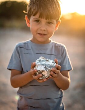 Curious Young Boy Holding Large Rock Outdoors at Sunset