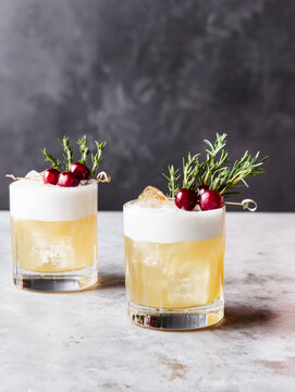classic whiskey sour cocktail with cranberry and rosemary garnish