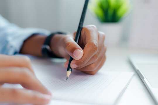 a person hand writing with black pencil on lined notebook paper, taking notes, creative writing, document signing, education and deep focus concept.