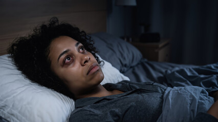 Obraz premium African american woman insomniac lying in bed at night with tired eyes looking up. Sleep disorder and mental health awareness