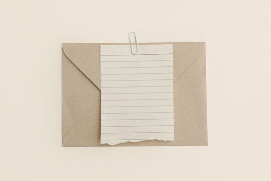 Vintage Kraft Envelope, Torn Lined Note Paper Scrap, White Paper Clip. Neutral Beige Table Background. Minimal Stationery Mockup for Letter, Message, Invitation, Branding. Office Design. Flatlay, top