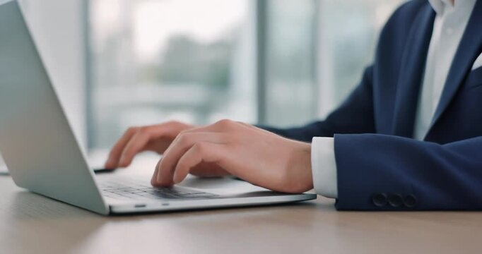 Businessman in blue suit typing on silver laptop keyboard