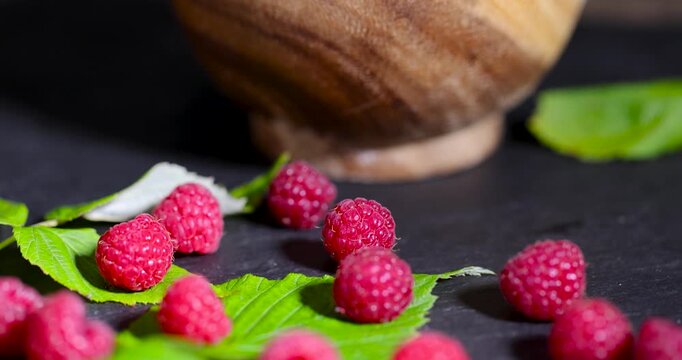 Summer raspberries on fresh green leaves, bushy raspberries are spread out on a black horizontal surface