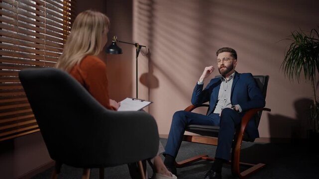 Casting director conducting audition for actors. Man auditioning in casting room. Male actor auditioning for main role. Movie producer holding folder. Man and woman having discussion at dim room.
